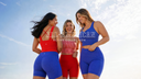 Three women wearing colorful  new AJ Activewear pieces in Red, blue Polka Dot and Red Gingham pattern with 'All-American Active Collection' text against a blue sky.