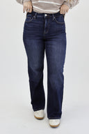 A person wearing dark blue straight-leg denim jeans, a beige and white striped sweater, and white sneakers, standing against a plain white studio background.